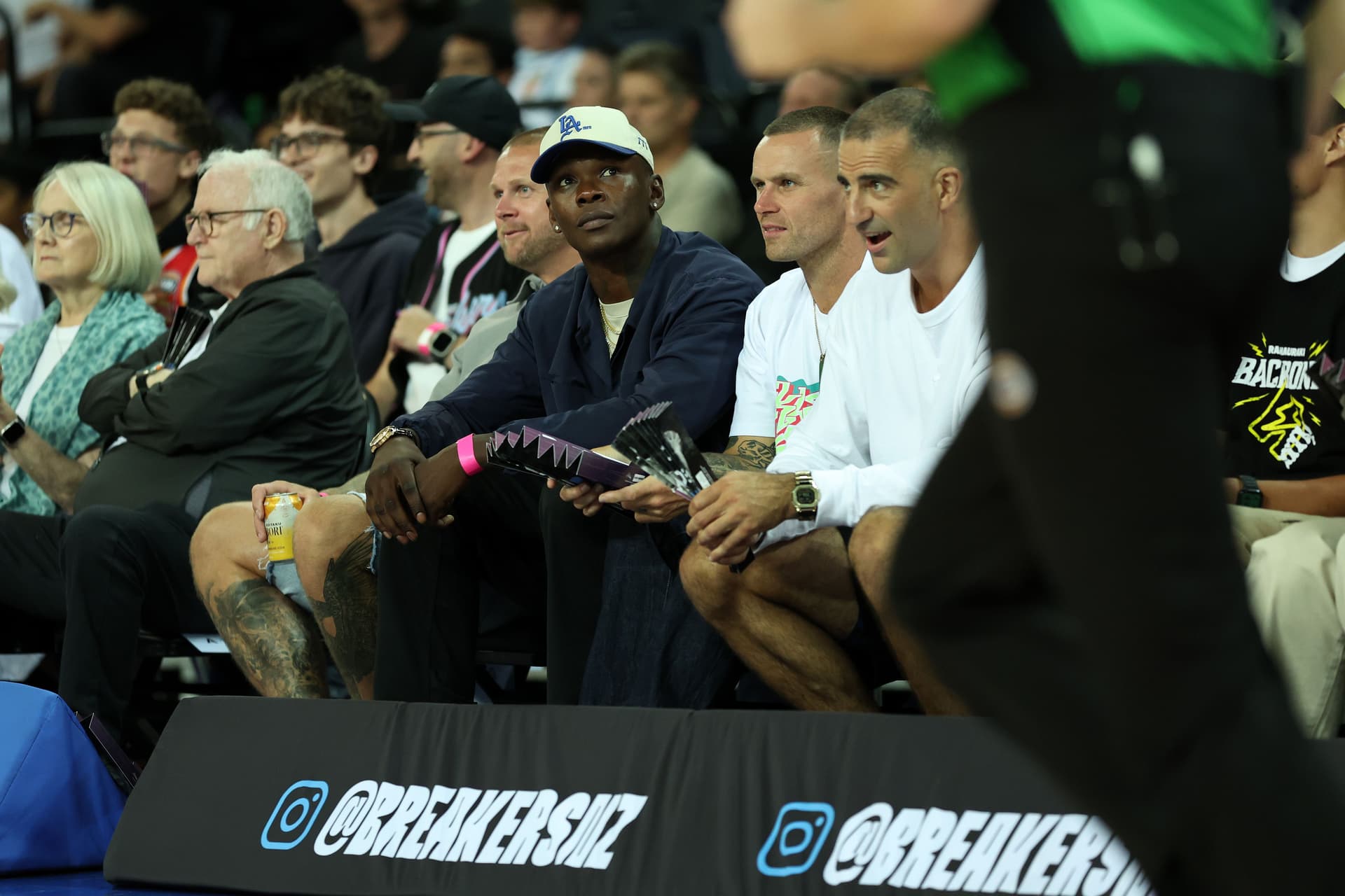 Mixed martial artist Israel Adesanya (C) watches during the round 18 NBL match